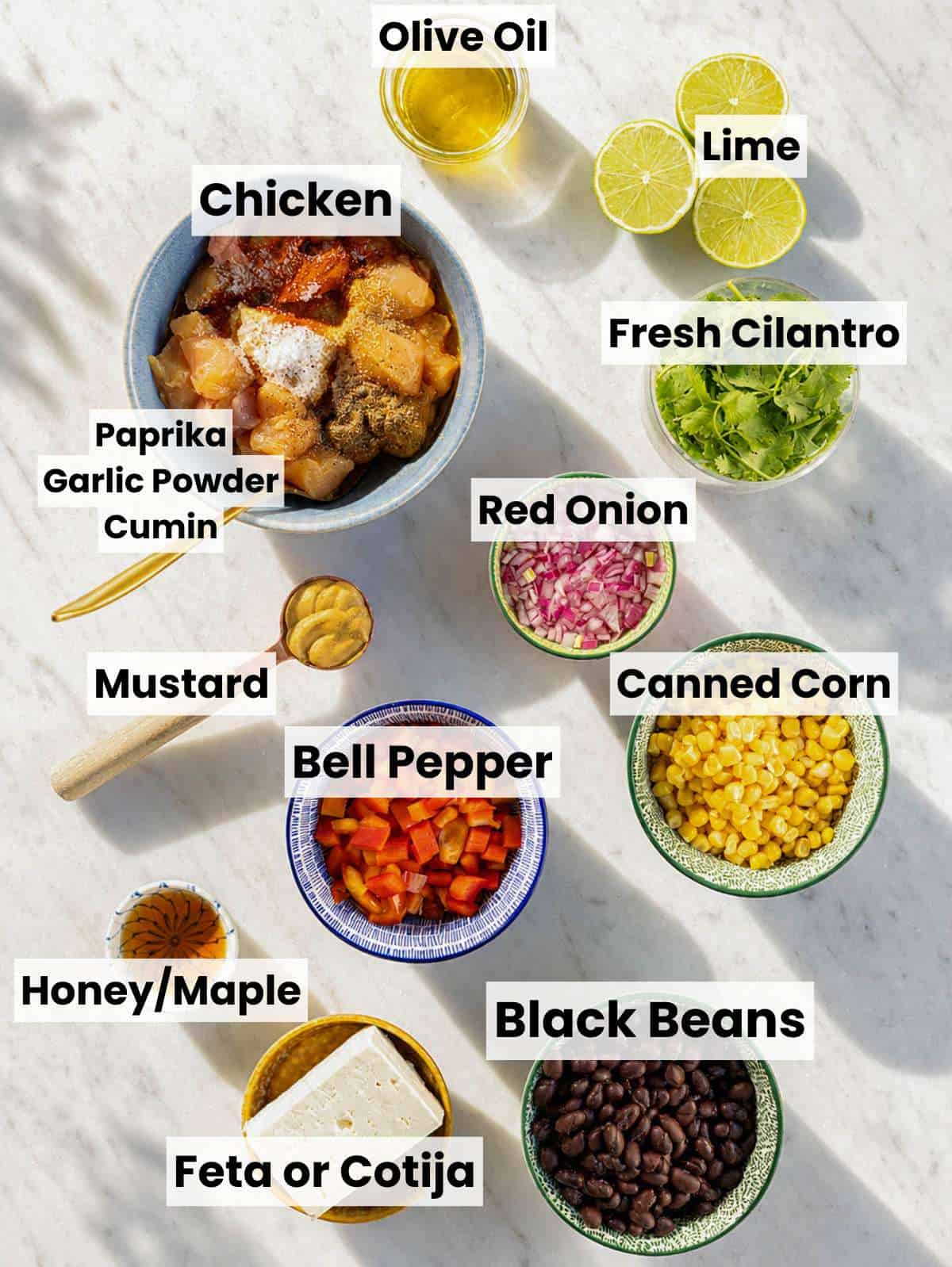 Ingredients for chicken black bean salad arranged on marble counter near bright kitchen window.