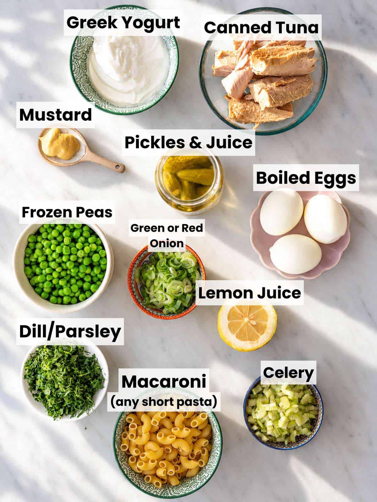 Ingredients for tuna macaroni salad arranged on a marble counter in natural window light.