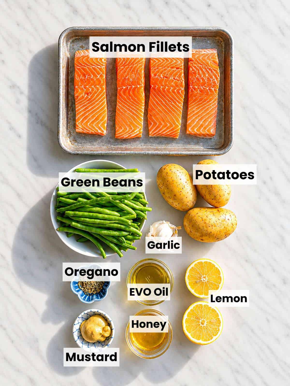 Salmon fillets, potatoes, green beans, lemon, honey, mustard, and garlic on marble surface.
