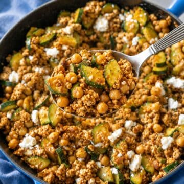 Skillet of ground turkey, zucchini, chickpeas, and feta with a rustic silver spoon.