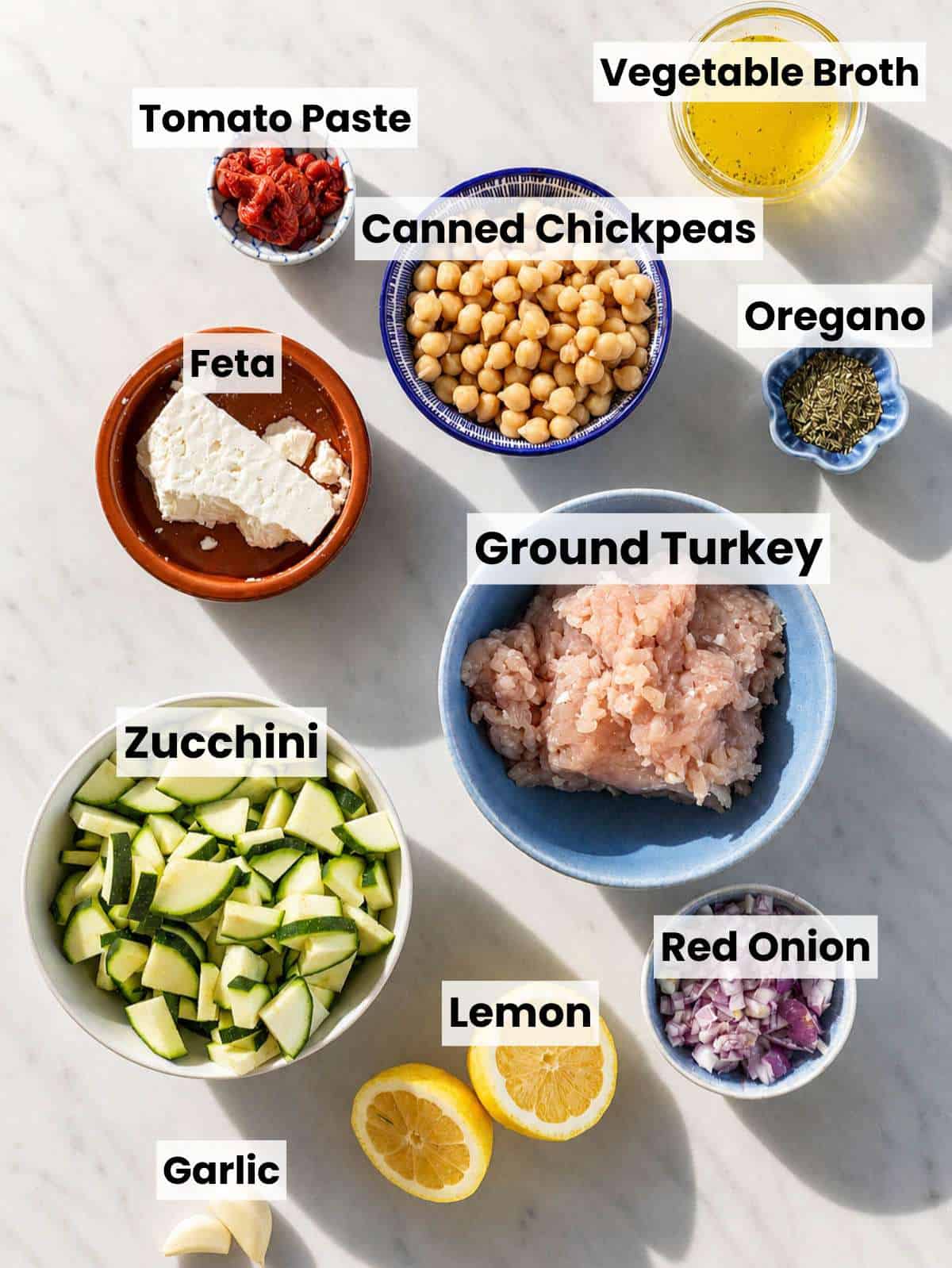 Small bowls of spices, chickpeas, zucchini, turkey, and feta on white marble counter.