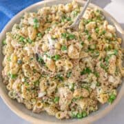 Spoon lifting creamy tuna macaroni salad with eggs and peas in natural light.