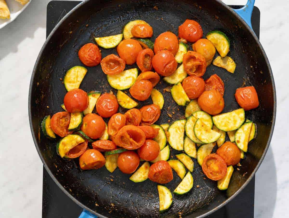 Step 2 Cherry tomatoes blistering in a skillet with sliced zucchini and grated garlic.