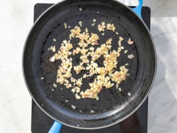 Step 2 Chopped red onion cooking in olive oil inside large skillet on marble countertop.