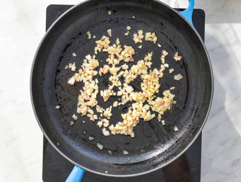 Step 2 Chopped red onion cooking in olive oil inside large skillet on marble countertop.