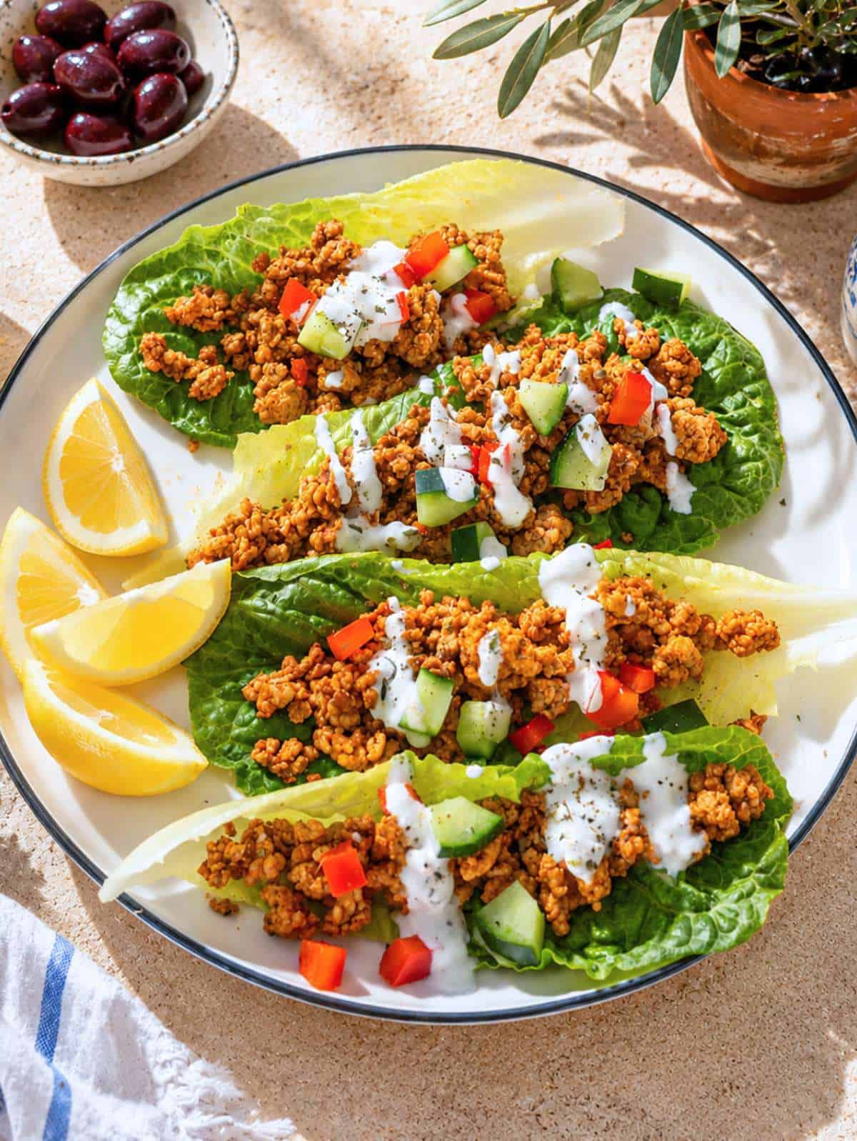 Turkey Lettuce Wraps topped with feta, cucumber, herbs, and creamy yogurt sauce on ceramic surface.