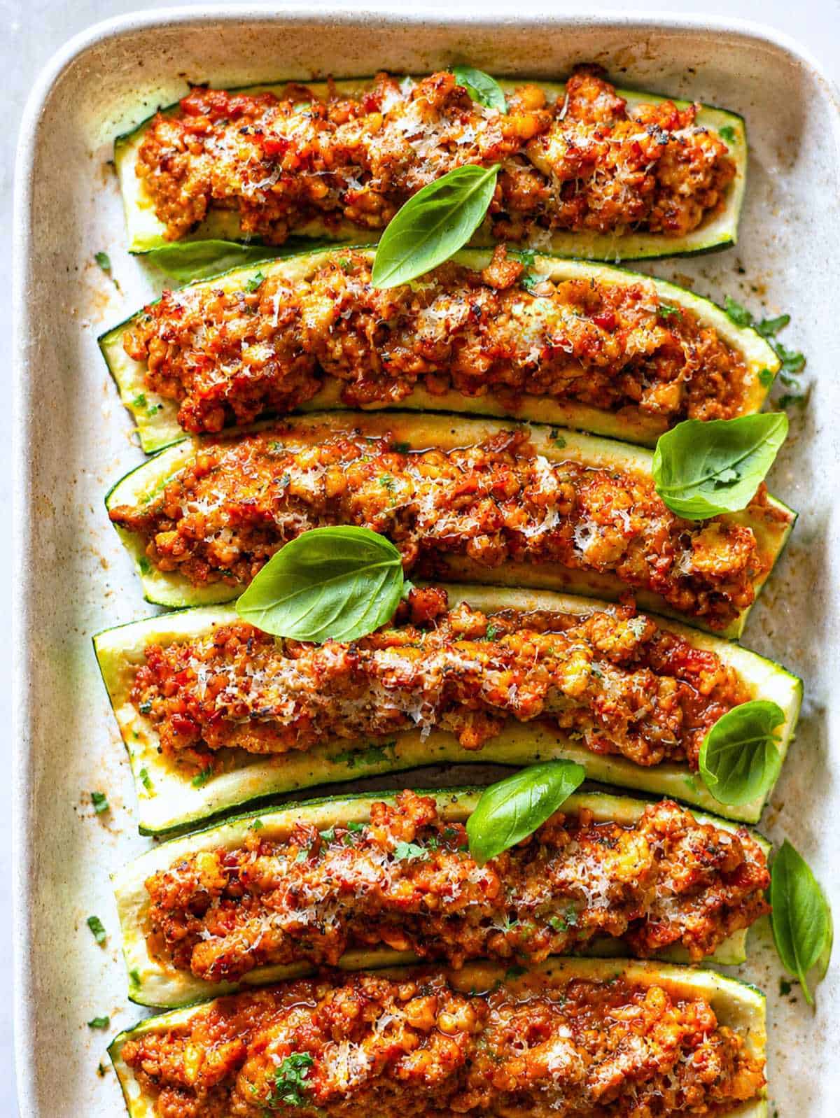 Baked turkey zucchini boats topped with Parmesan, fresh basil, and lemon zest on a silver tray.