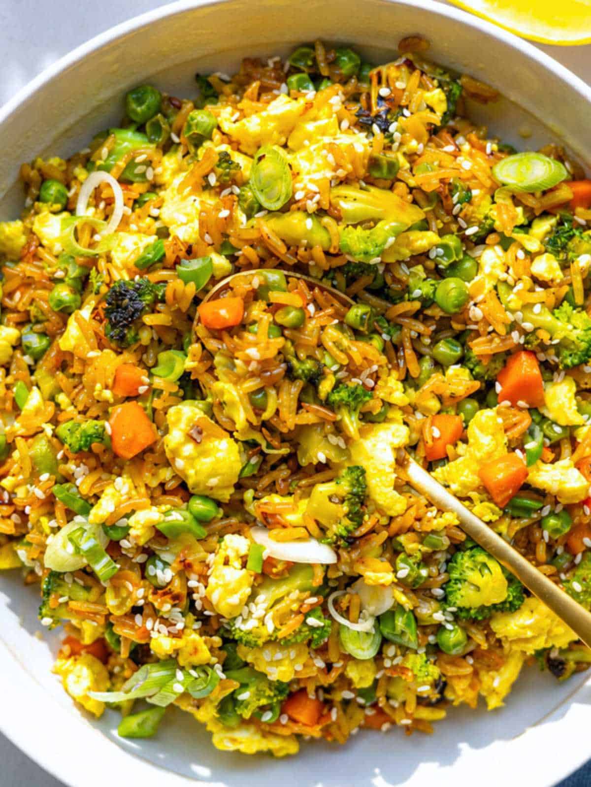 Bowl of egg fried rice with broccoli, peas, carrots, scallions, and fluffy scrambled eggs.