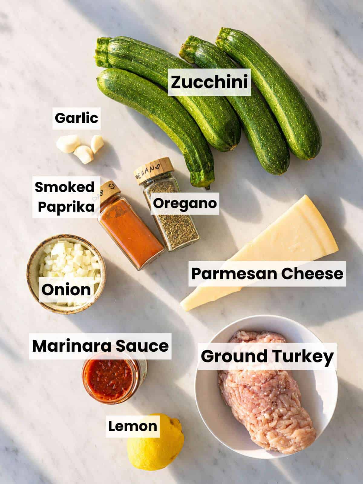 Ingredients for turkey zucchini boats with ground turkey, zucchini, marinara, Parmesan, onion, and garlic.