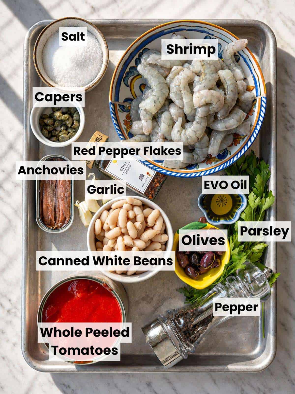 Shrimp, capers, tomatoes, cannellini beans and other ingredients on a table.